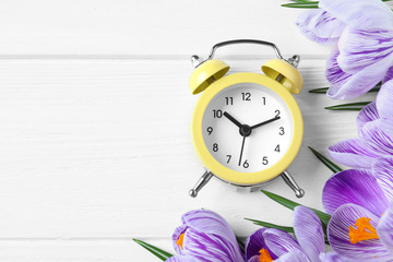 Yellow alarm clock, spring flowers and space for text on white wooden table, flat lay. Time change