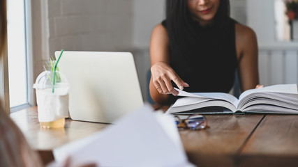 Cropped image of young beautiful women tutoring/reading a books while sitting together at the wooden table over vintage living room as background.