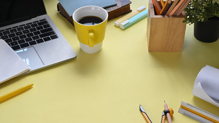Top view image of colorful workplace that full of document, pencil compass, coffee cup, notebook, pencil holder, marker pens, potted plant and computer laptop with black empty screen.