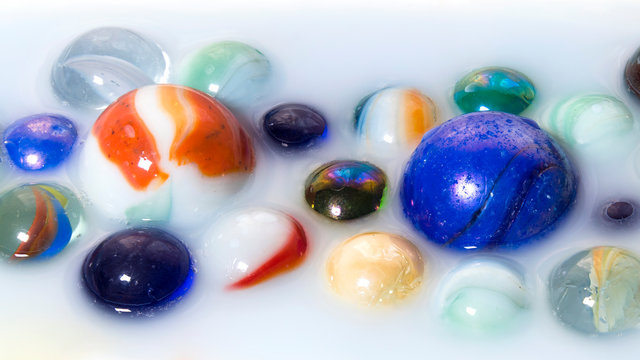 Multicolored marbles inside milk as abstract background