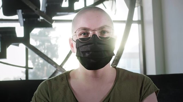 Bald girl is sick with cancer. Woman puts on a medical protective black mask. Protects against Chinese coronavirus. Rehabilitation after chemotherapy. HIV is infected. Pandemic insurance coronavirus.
