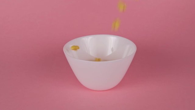 Breakfast cereal pours into a deep white plate on a pink background, slow motion.