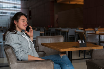 A young girl is smiling and talking on a cell phone in a cafe or restaurant. Horizontal side view.