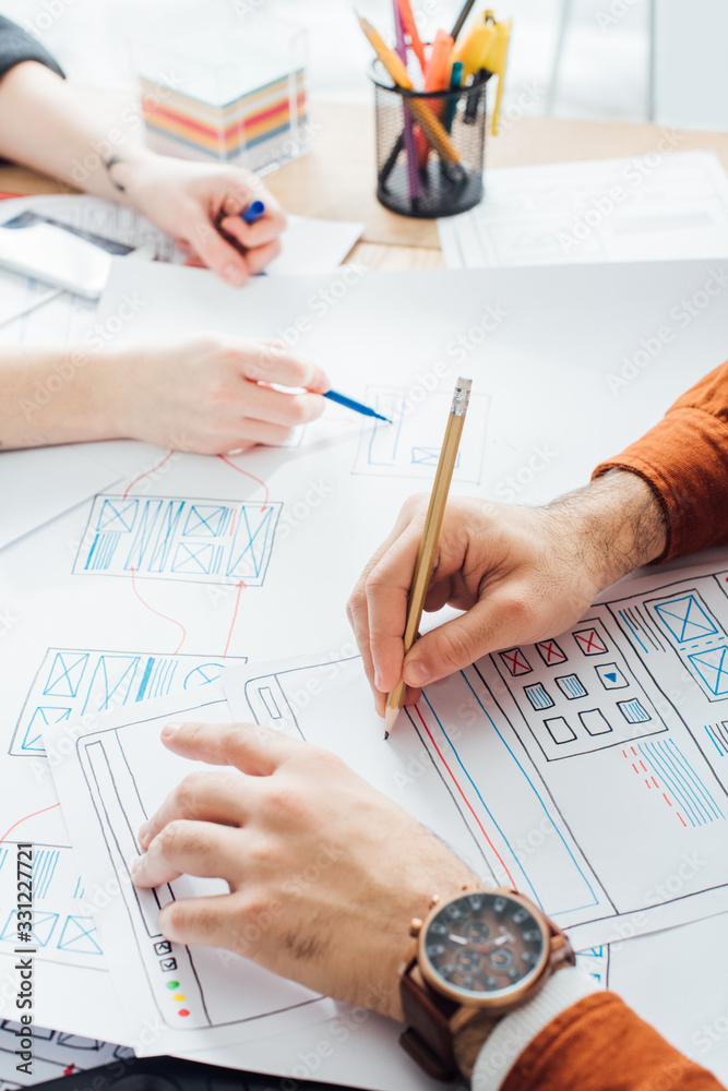 Wall mural cropped view of ux designer holding pencil while planning sketch applications near colleague at tabl