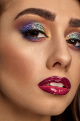 Naklejka premium Brunette female with luxury makeup and perfect skin is looking at you. Multi-colored eyeshadow, false eyelashes, glossy burgundy lips. Close up
