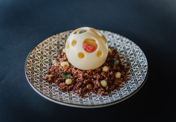 Biscuit cake in chocolate sphere, with Bulgarian rose jam, on a sofa of cocoa biscuits and rose sugar