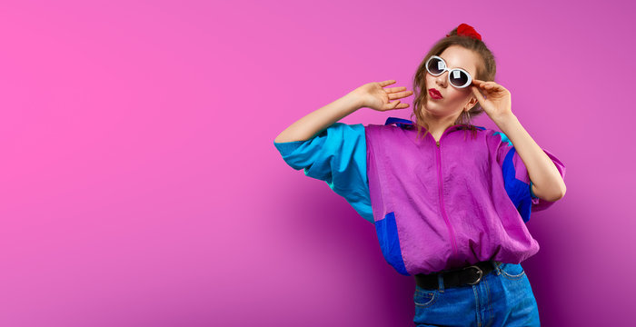 Cool teenager. Fashionable DJ girl in colorful trendy jacket and vintage retro sunglasses enjoys style of 80s � 90s vibes. Teenager Girl at disco party. Young fashion model on pink color background.