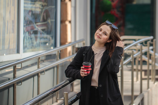 cheerful woman on a city street drinks coffee on a sunny day and looks at the camera. coffee to go. Portrait of a girl with a drink in hands