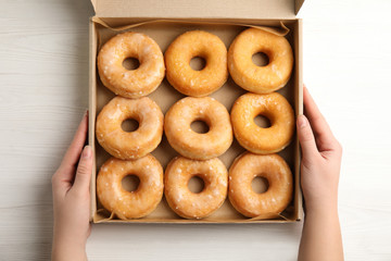 Woman with box of delicious donuts at white wooden table, top view