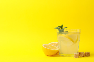 Lemonade, lemons and sugar cubes on yellow background, space for text