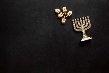 Jewish holiday Hanukkah with menorah - traditional Candelabra - and wooden dreidels spinning top. Black background, top view, copy space