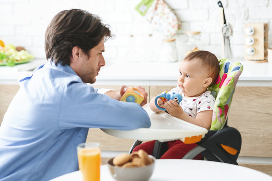 Curious Baby In High Chair Playing With Daddy At Kitchen