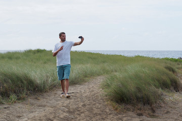 Man video blogger walks along a path in the  green grass near ocean. Tropical island, coastline. Lifestyle.