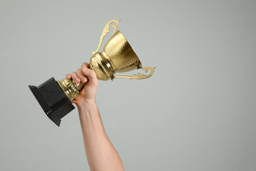 Man holding gold trophy cup on light grey background, closeup. Space for text - obrazy, fototapety, plakaty