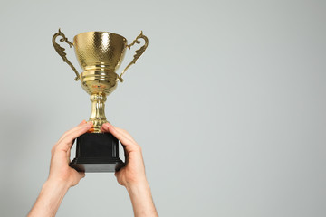 Man holding gold trophy cup on light grey background, closeup. Space for text