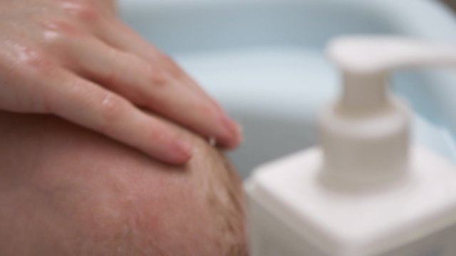 Moher hand gently washing newborn baby head. Close up slow motion shot