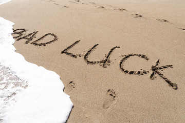 English word 'bad luck' written on the sand beach washing away by bubble ocean wave.