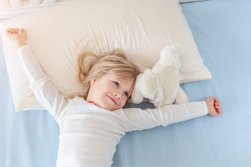 Cute adorable caucasian blond little toddler kid girl lying in bed on white pillow. Adorable sweet...