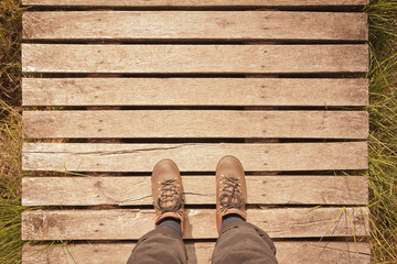 Hiking boots on a wooden boardwalk with copy space, pov concept, vintage filter effect.