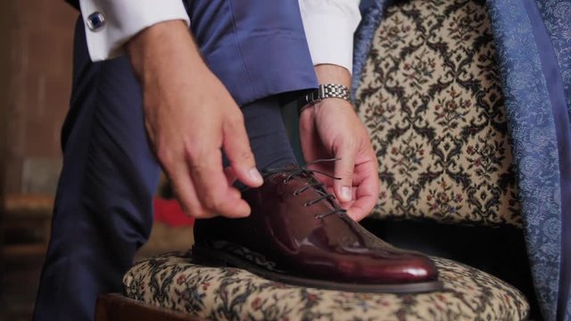 Elegant man tying his lace on his shiny shoes. His foot is on a vintage chair.Slow motion Full HD