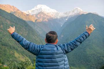 Back view of Middle-aged man raised his hands and looking to beautiful view of Annapurna mountains range in the morning. Annapurna Region is the most diverse and popular trekking area in Nepal.