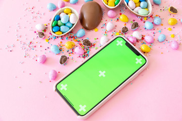 Phone with green screen, stylish easter eggs on pink paper flat lay, space for text. Happy Easter. Greeting card template.	