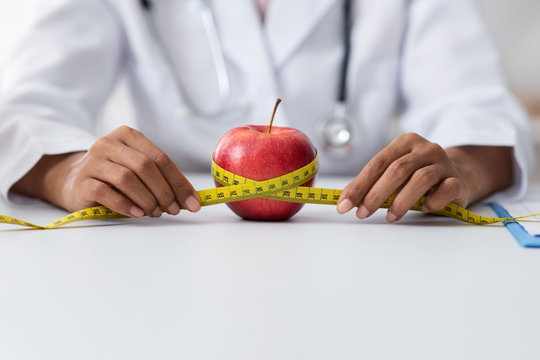 Dietitian black woman holding red apple and measuring