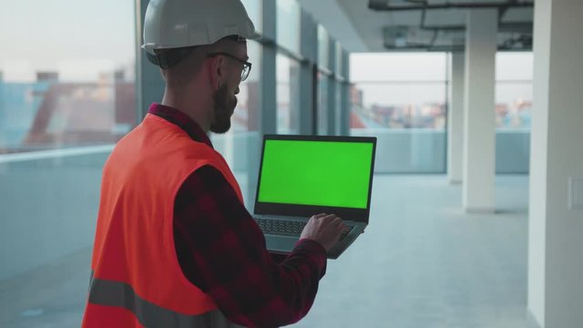 Inside in building man engineer stand using laptop computer with green screen worker project occupation builder technology mock-up professional male safety device computer slow motion