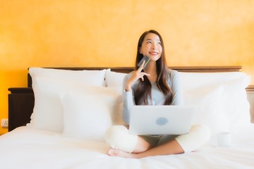 Portrait beautiful young asian woman using computer notebook or laptop with credit card on bed