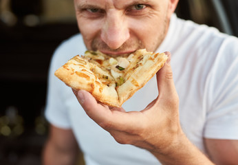 Close up view of hungry man eating piece of pizza