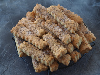 Home cooking. Shortbread Sticks sprinkled with sugar and poppy seeds on a metal grate on a dark background. Close-up.