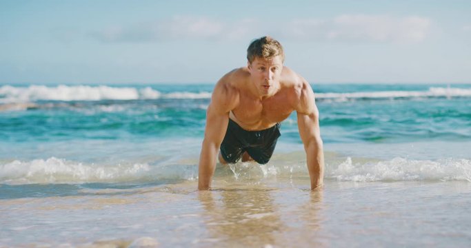 Strong muscular man doing push ups on the beach in the morning, fit young man working out