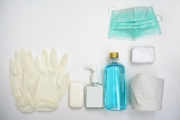 A pair of white rubber gloves, soap, pump bottle, alcohol, tissue role, cotton patches and face mask on white background.  Objects for Coronavirus or Covid 19 protection.  Flat lay.