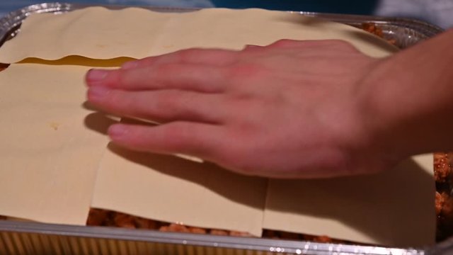 Homemade preparation of lasagna. Close-up image of the pan: the hands are arranging the pasta sheets, layer by layer, and then seasoning them with meat sauce and bechamel.