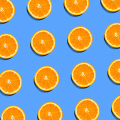 Tropical summer pattern of fresh orange slices on blue background. Top view of cross section of colorful citrus fruit. Contrasting flat lay composition.
