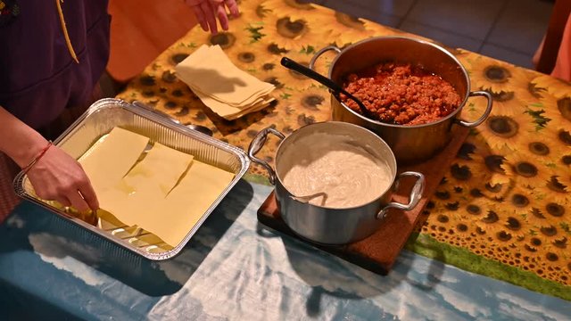 Homemade preparation of lasagna. The hands of a Caucasian woman are placing the sheets of puff pastry in the pan.