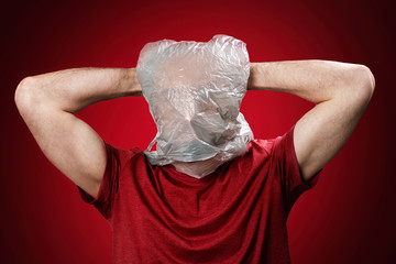 The man holds his head in his hands, suffocating in a plastic bag. Red background. Copy space. Concept of pollution and environmental protection