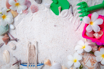Toys kid with sea shells and plumeria flowers on sand background
