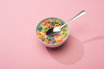 bright colorful breakfast cereal with milk in bowl with spoon on pink background