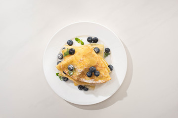 top view of tasty crepes with blueberries and mint on plate on grey background