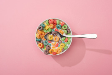 top view of bright colorful breakfast cereal in bowl with spoon on pink background