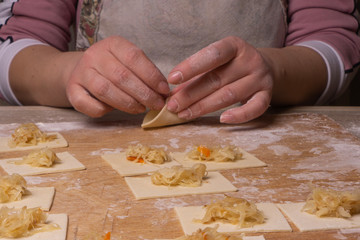 A woman sculpts dumplings and ravioli from squares of dough and cabbage. Plywood cutting board, wooden flour sieve and wooden rolling pin - tools for making dough.