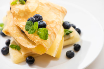 close up view of tasty crepes with mint and blueberries on plate on white background
