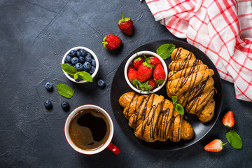 Croissant with fresh berries and cup of coffee on black.