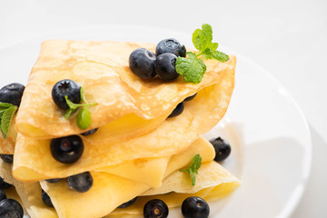 close up view of tasty crepes with mint and blueberries on plate on white background