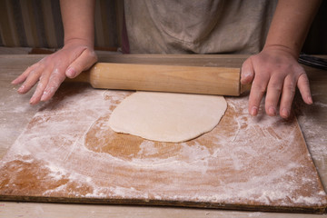 A woman rolls out the dough. Plywood cutting board, wooden flour sieve and wooden rolling pin - tools for making dough.