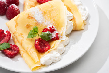 close up view of tasty crepes with raspberries and whipped cream on plate
