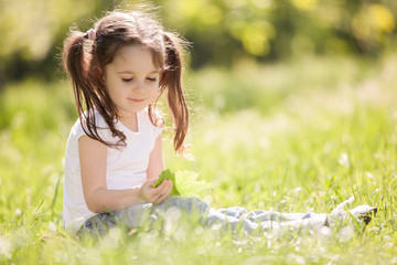 Naklejka na ściany i meble Cute little girl play in the park. Beauty nature scene with colorful background at summer or spring season. Family outdoor lifestyle. Happy girl relax on green grass