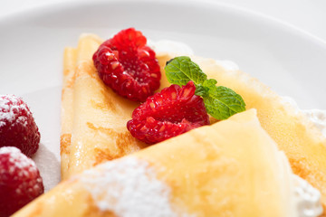 close up view of tasty crepes with raspberries and whipped cream on plate