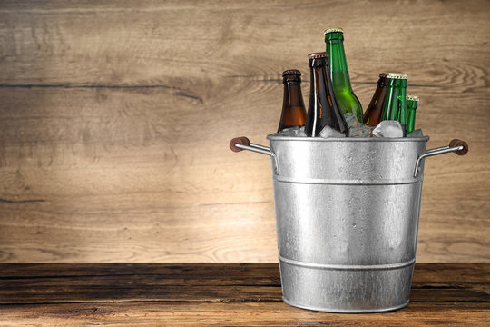 Metal bucket with beer and ice cubes on wooden table. Space for text